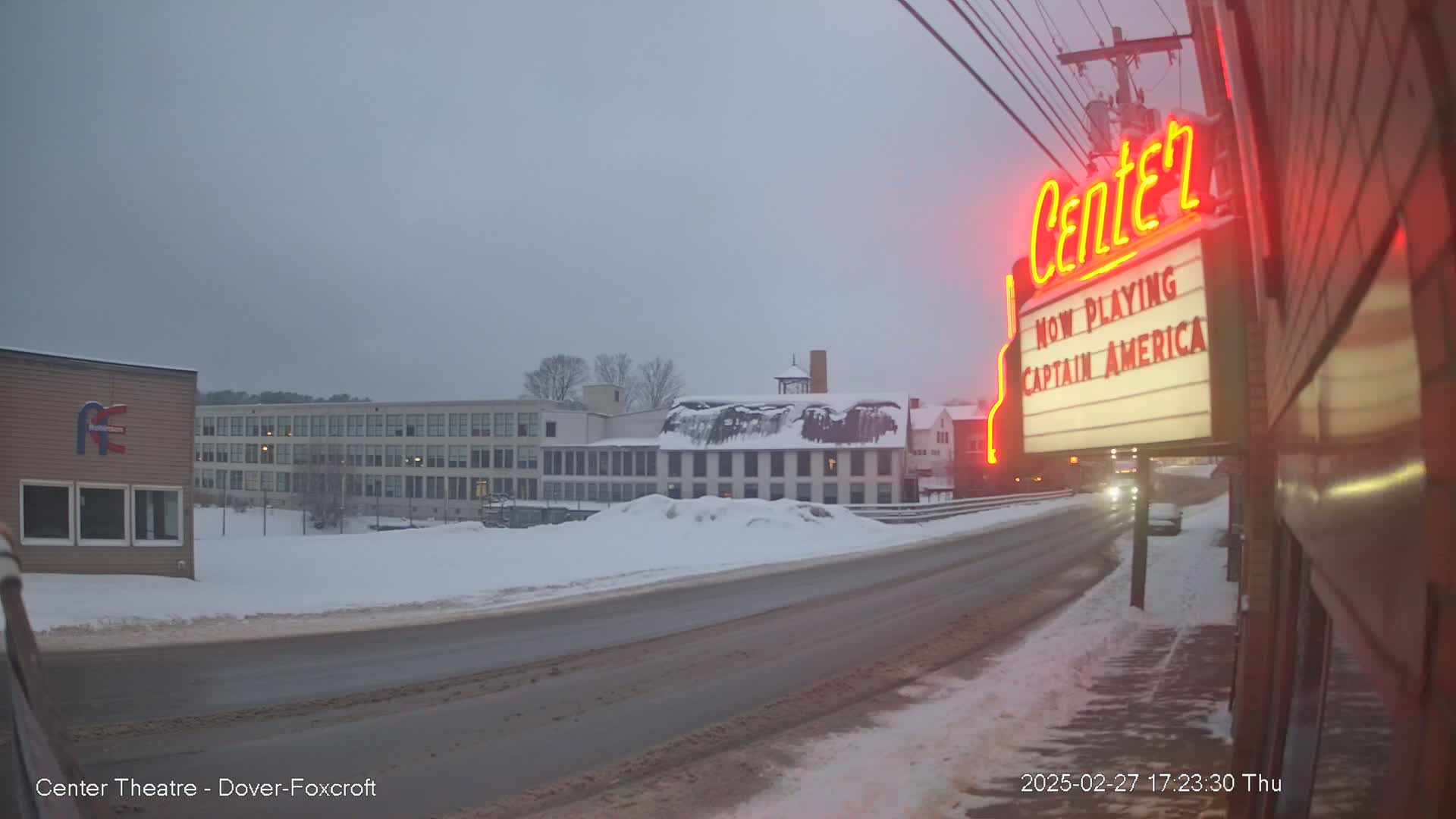 A snow-covered street scene shows a movie theater marquee advertising "Captain America," a multi-story building in the background, and a road with some vehicles.