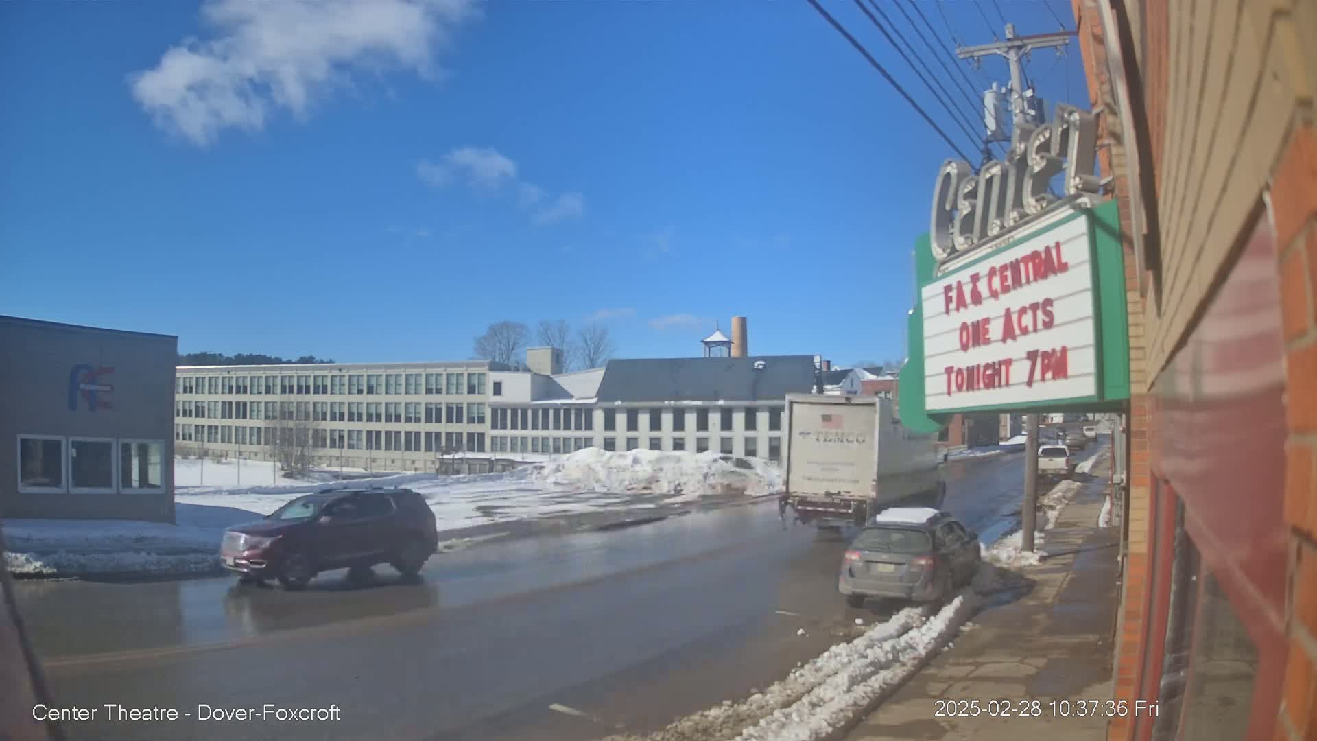 A mostly sunny day reveals a street scene with melting snow, several cars, a large building, and a theater marquee.