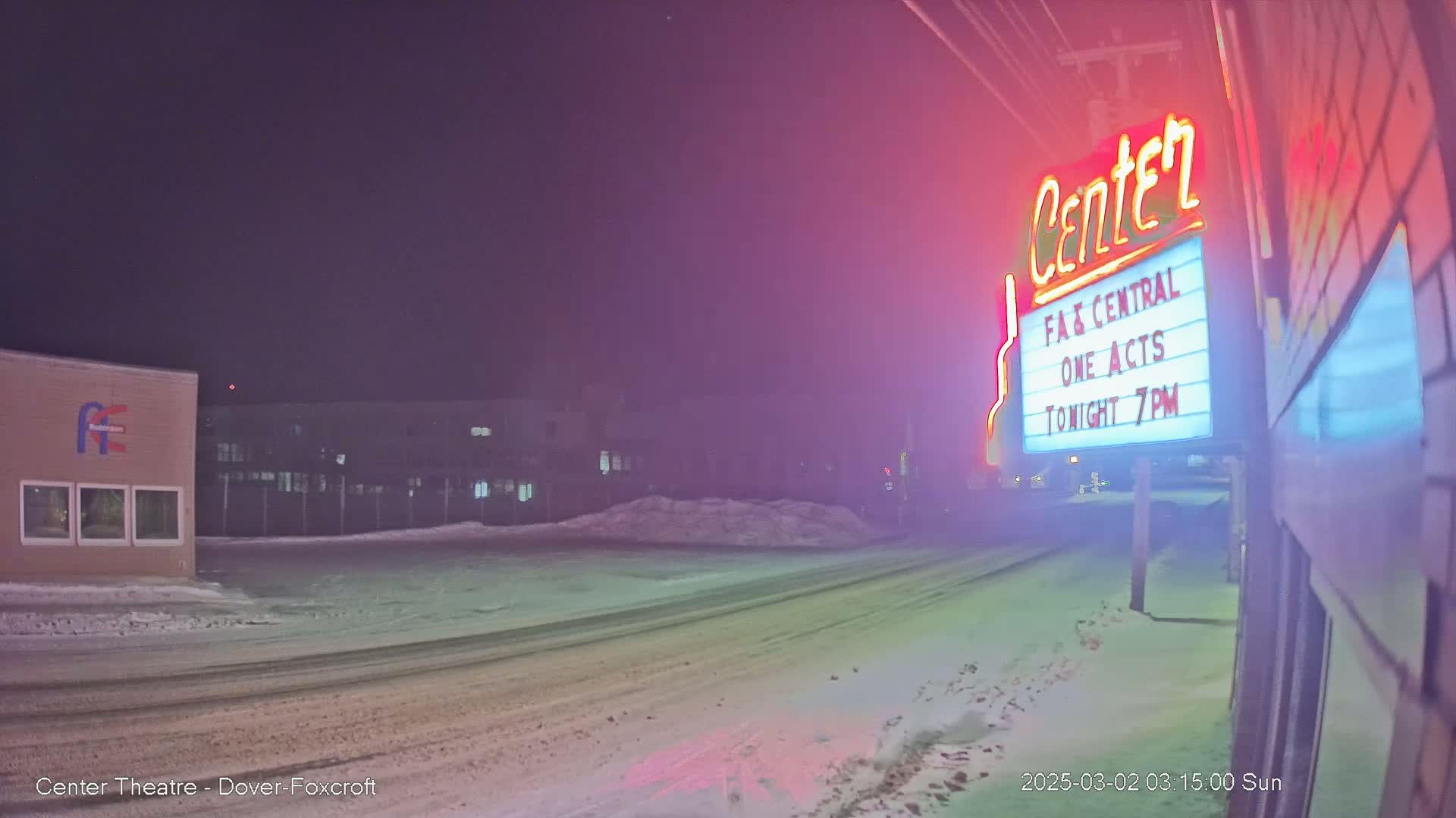 A snow-covered street at night, illuminated by a brightly lit theater marquee.