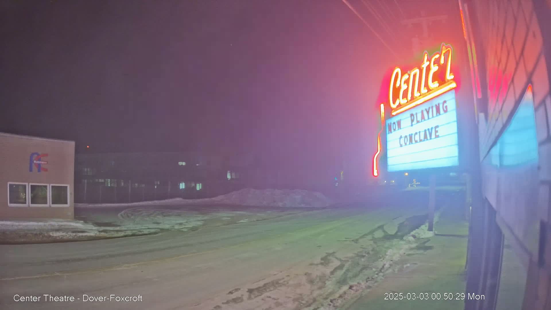 A snowy, foggy night scene shows a movie theater marquee advertising "Conclave," with a building in the background.