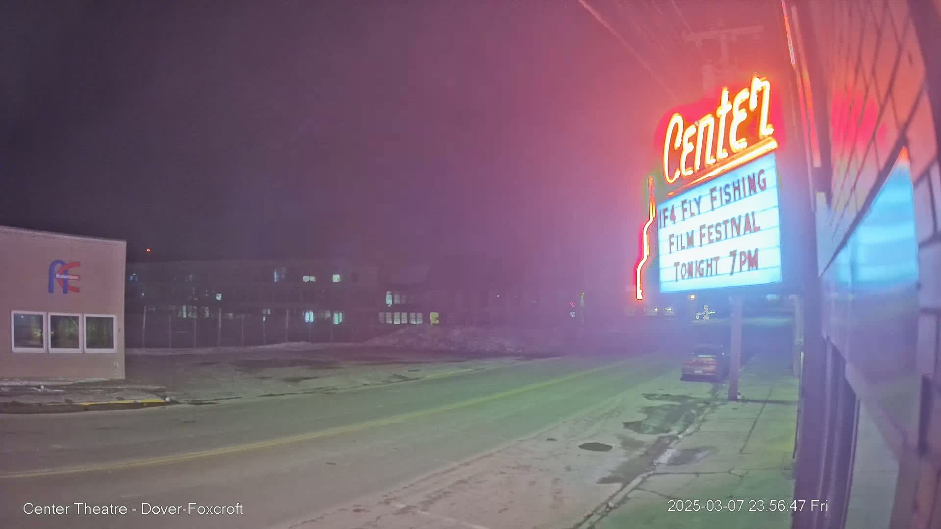 A nighttime street scene shows a road with a building and a neon sign advertising a film festival.