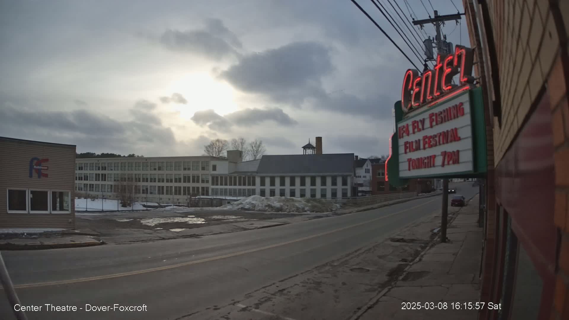 A mostly cloudy sky brightens over a town street with buildings and a marquee advertising a film festival.