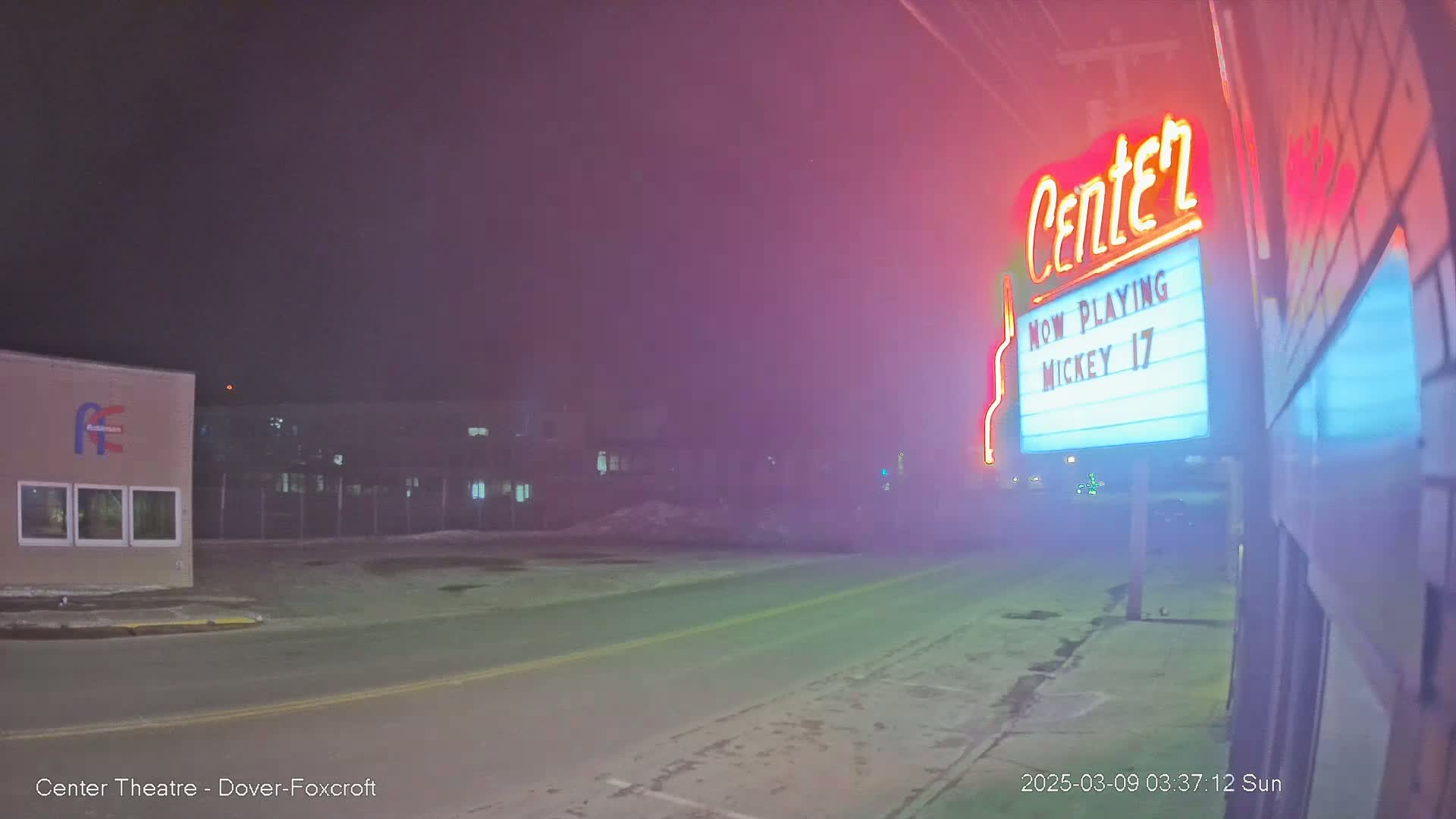 A fog-shrouded night scene shows a street in front of a movie theater marquee advertising "Mickey 17."