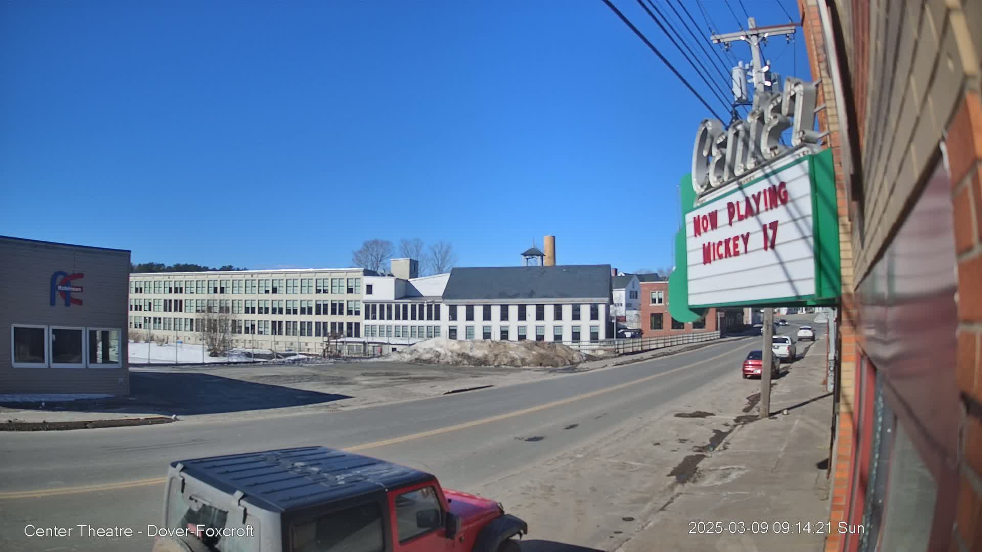 A sunny day reveals a street scene with several multi-story buildings, a few parked cars, and a red Jeep in the foreground.