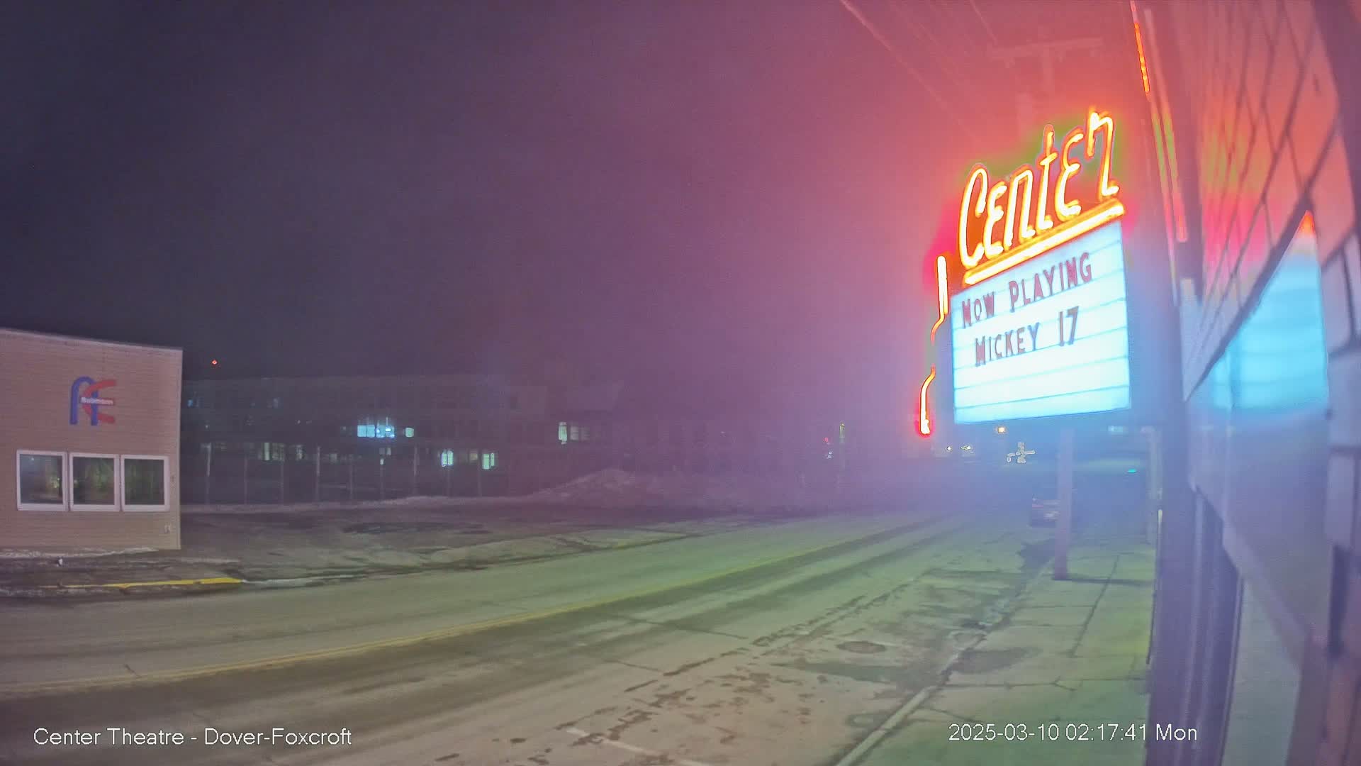 A foggy night scene shows a movie theater marquee advertising "Mickey 17," with a street and buildings visible in the background.