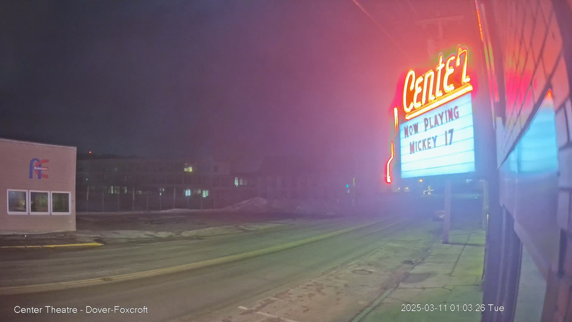 A foggy night scene shows a movie theater marquee displaying "Mickey 17" with a road and buildings in the background.