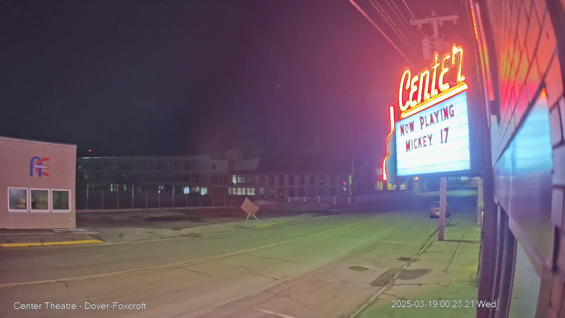 A nighttime street scene shows a movie theater marquee advertising "Mickey 17," with buildings and a mostly clear sky visible in the background.