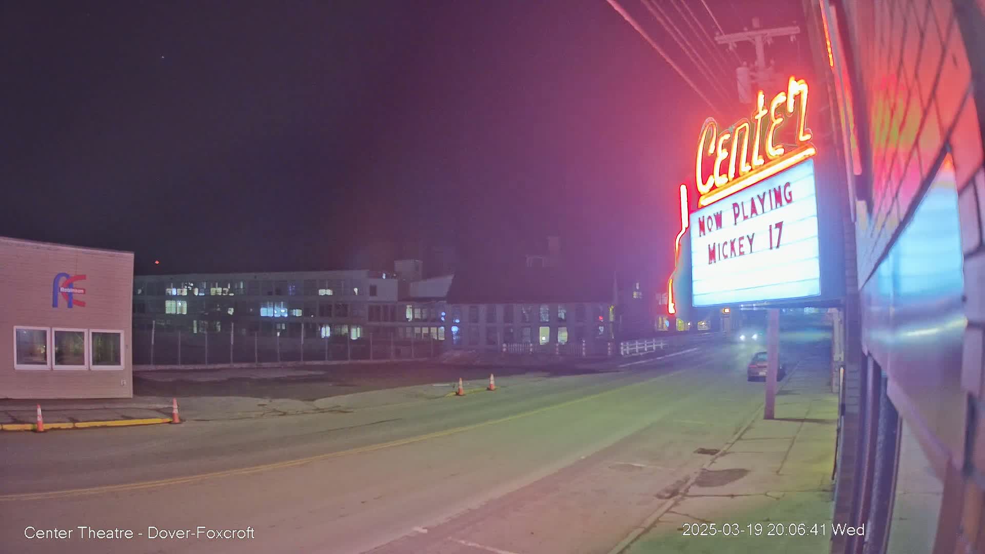 A nighttime street scene shows a neon-lit theater marquee and a mostly empty road under a dark, clear sky.