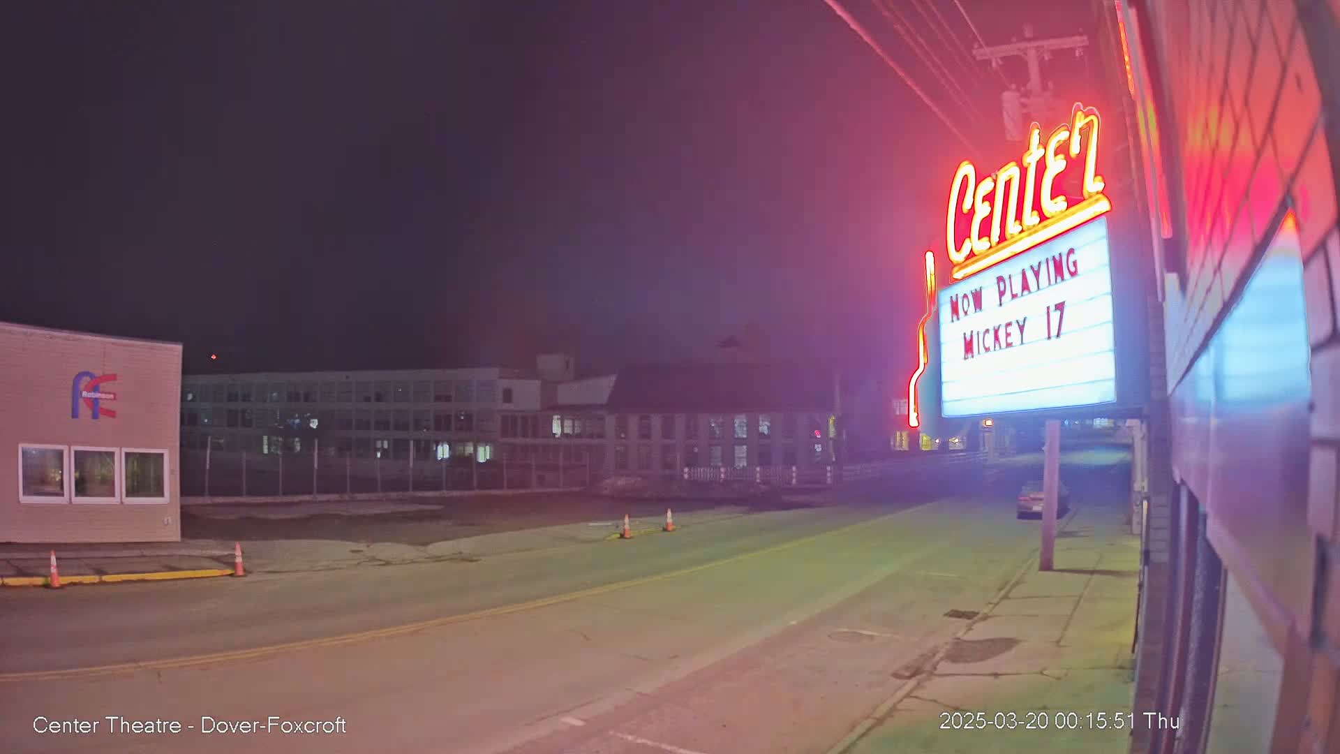 A nighttime street scene shows a movie theater marquee advertising "Mickey 17," with a hazy or foggy atmosphere.