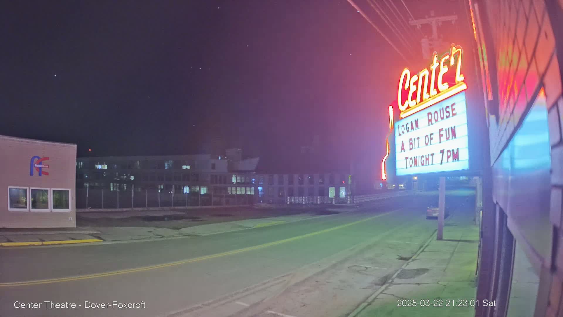 A nighttime street scene under a clear, starry sky shows a theater marquee advertising a show, a building across the street, and a vehicle parked nearby.