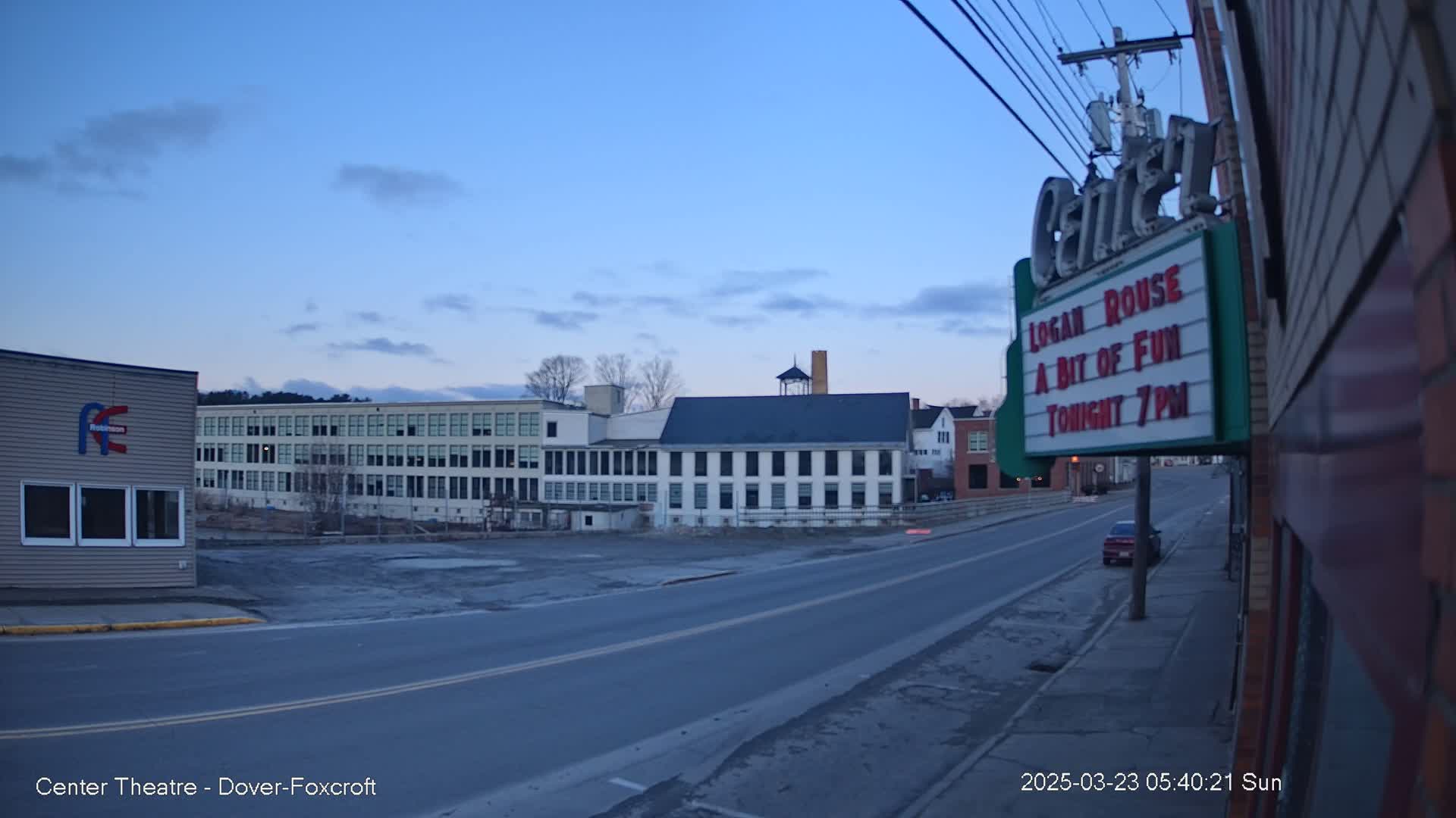 A mostly empty street at twilight, featuring several multi-story buildings, one of which is a theater displaying a marquee.