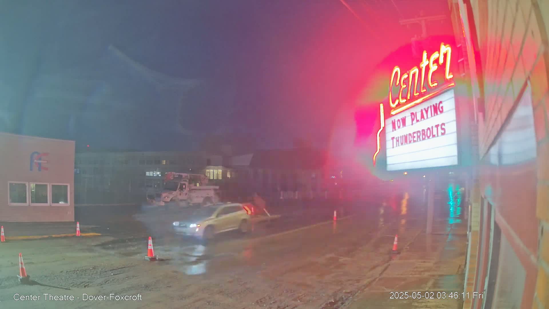 A rain-slicked street at night shows a car and a utility truck near a movie theater marquee that advertises "Thunderbolts."