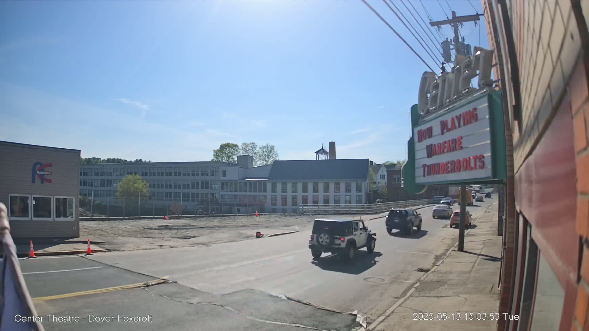 A sunny day shows a street scene with several cars driving past a large building,  and a movie theater marquee.