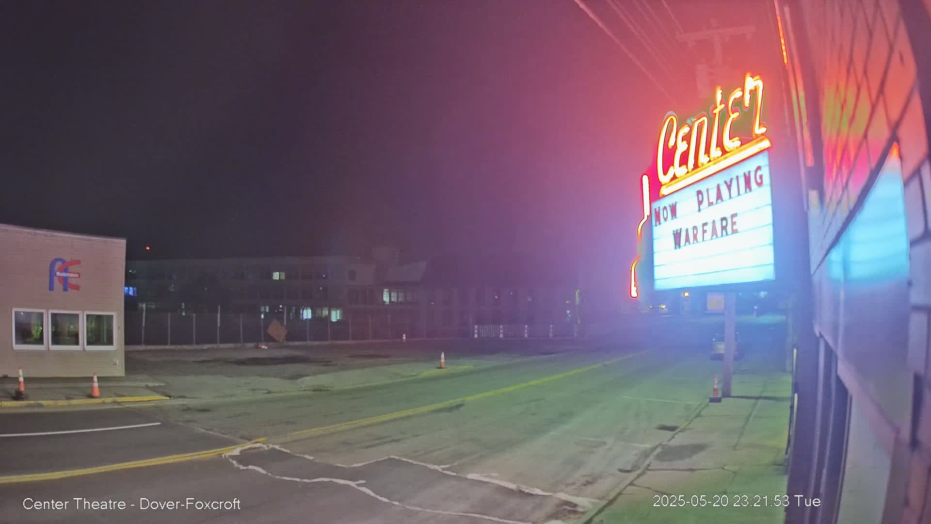 A nighttime, hazy view of a mostly empty street in front of a movie theater marquee advertising the film "Warfare."
