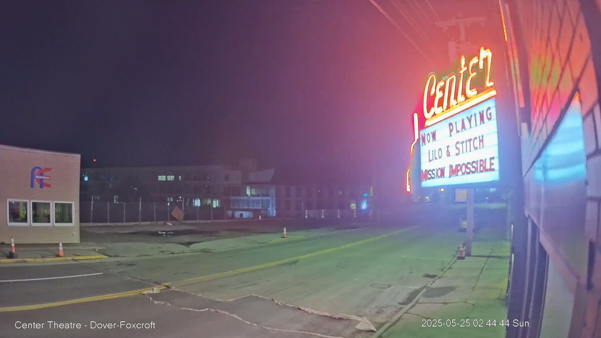 A nighttime street scene shows a movie theater marquee advertising "Lilo & Stitch" and "Mission Impossible," with a hazy atmosphere.