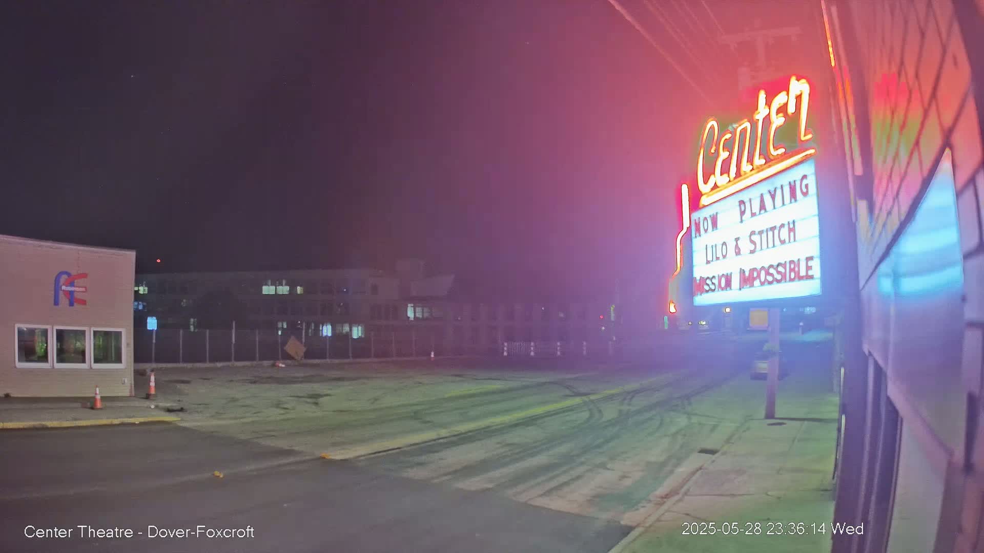 At night, a movie theater marquee advertises *Lilo & Stitch* and *Mission: Impossible*, while tire marks are visible on an empty lot in front of it.