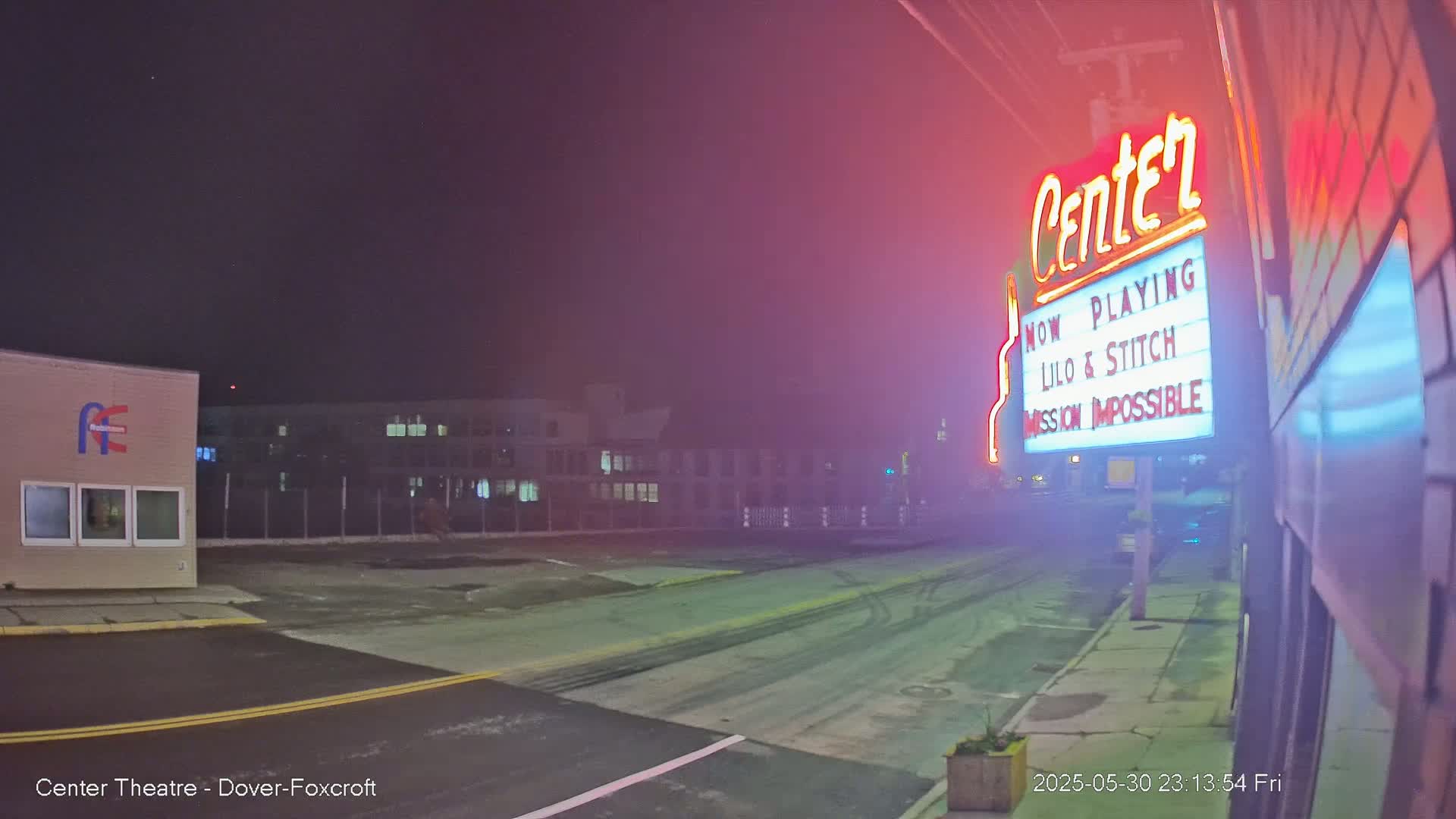 A nighttime street scene shows a movie theater marquee advertising Lilo & Stitch and Mission Impossible, with a hazy or foggy atmosphere.