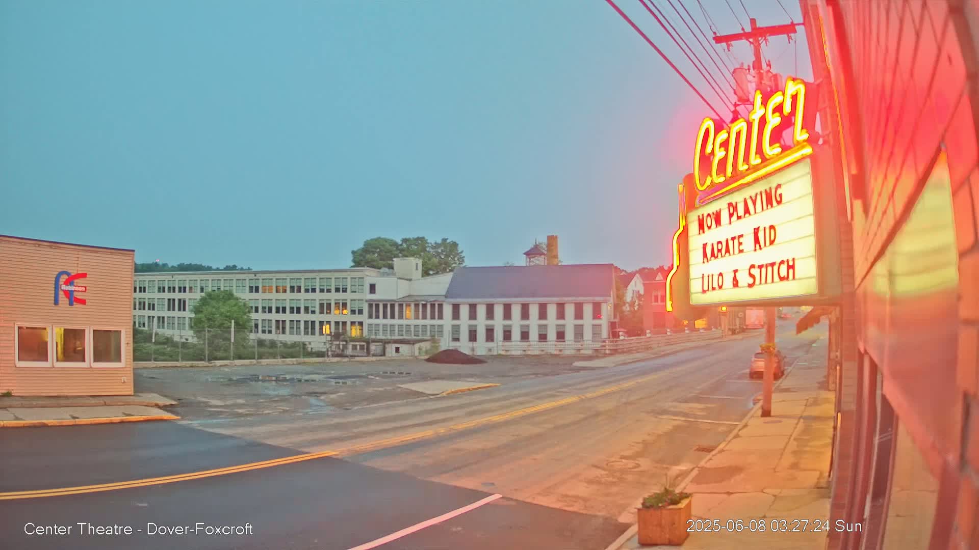 A street scene at dawn shows a movie theater marquee advertising "Karate Kid" and "Lilo & Stitch," with a large building across the street.