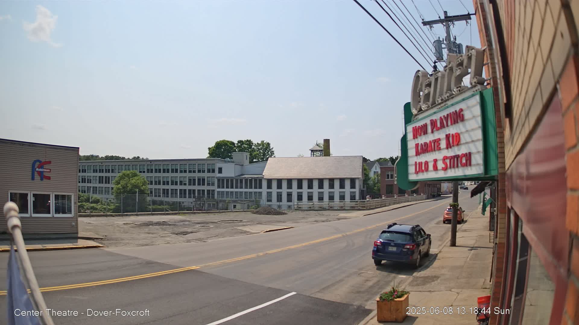 A sunny day reveals a street scene with a large, multi-story building across the road, and a smaller building to the left, with cars parked on the street.