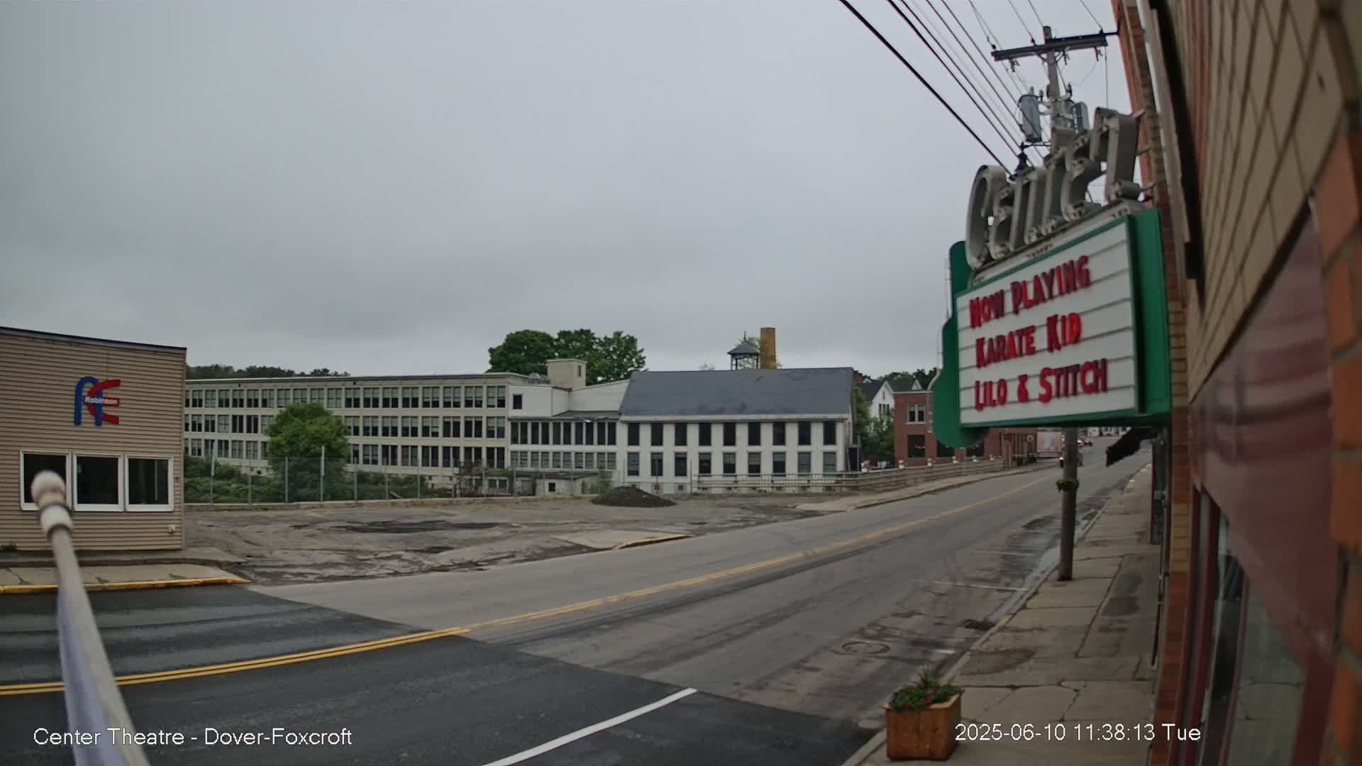 A mostly empty street stretches toward several industrial-style buildings under a gray, overcast sky.
