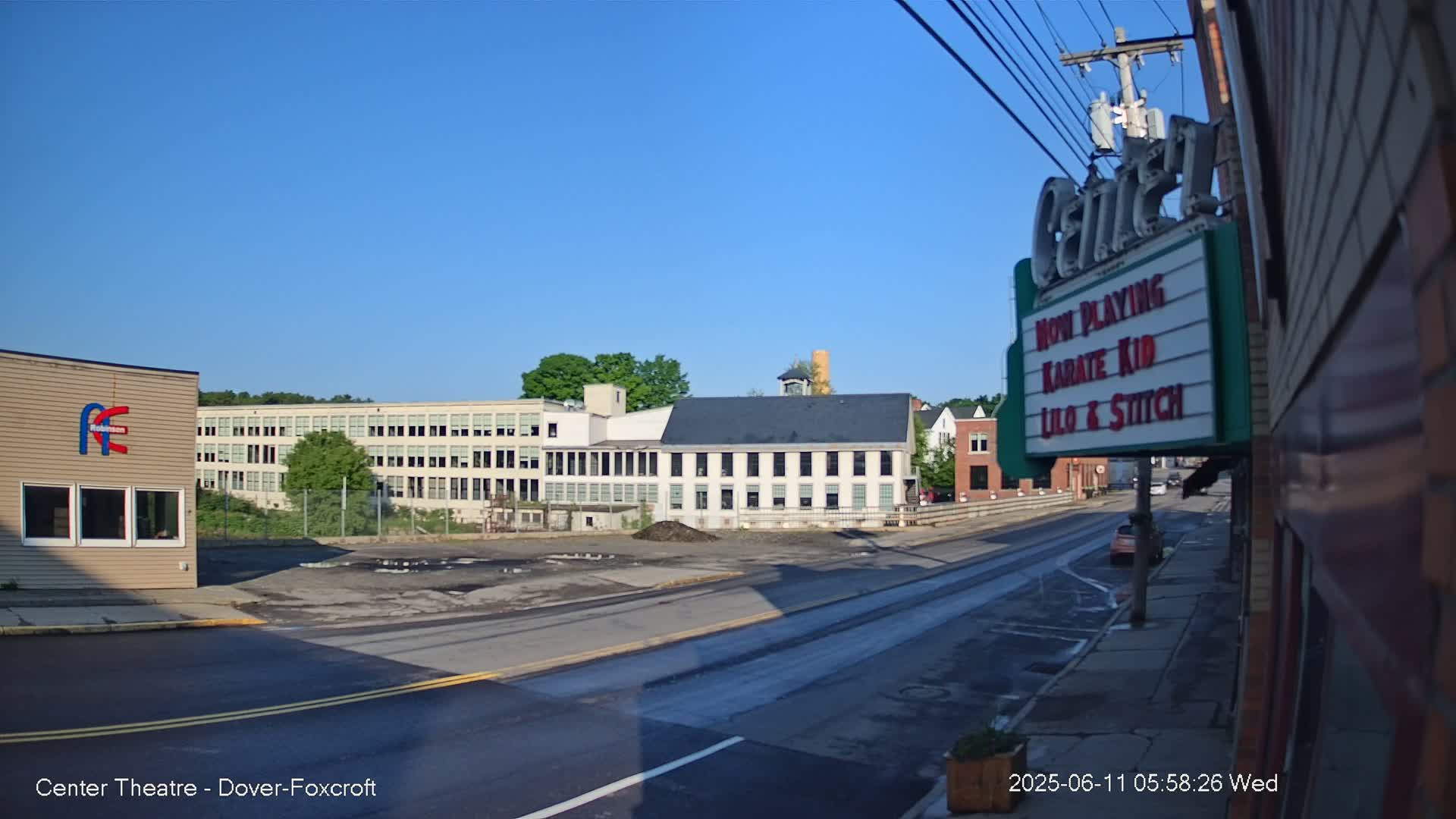 A street scene on a sunny day shows a long, multi-story building and a movie theater marquee.