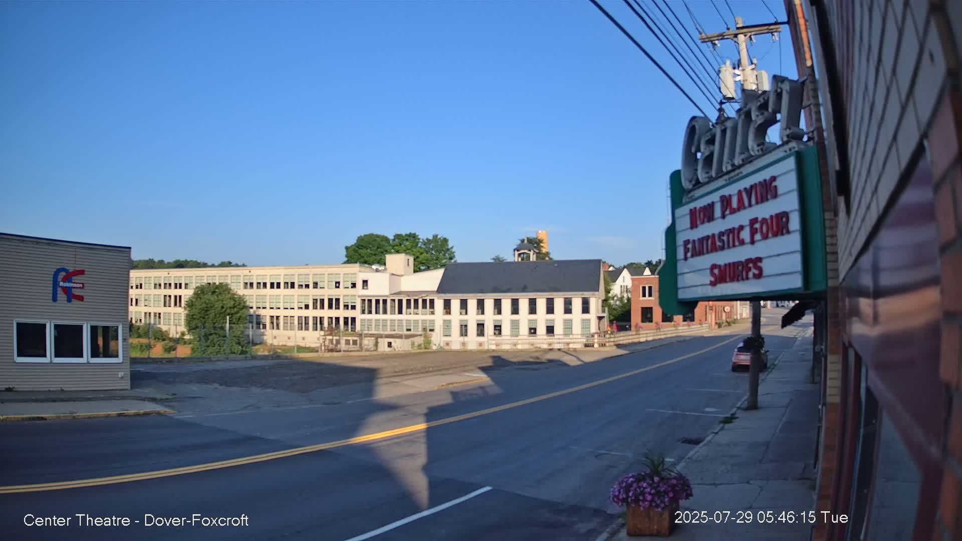 A nighttime, hazy street scene shows a movie theater marquee advertising "Superman" and "Smurfs," with a building and empty parking lot visible in the background.