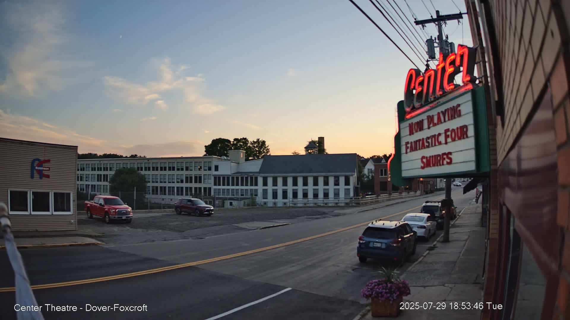 A nighttime, hazy street scene shows a movie theater marquee advertising "Superman" and "Smurfs," with a building and empty parking lot visible in the background.