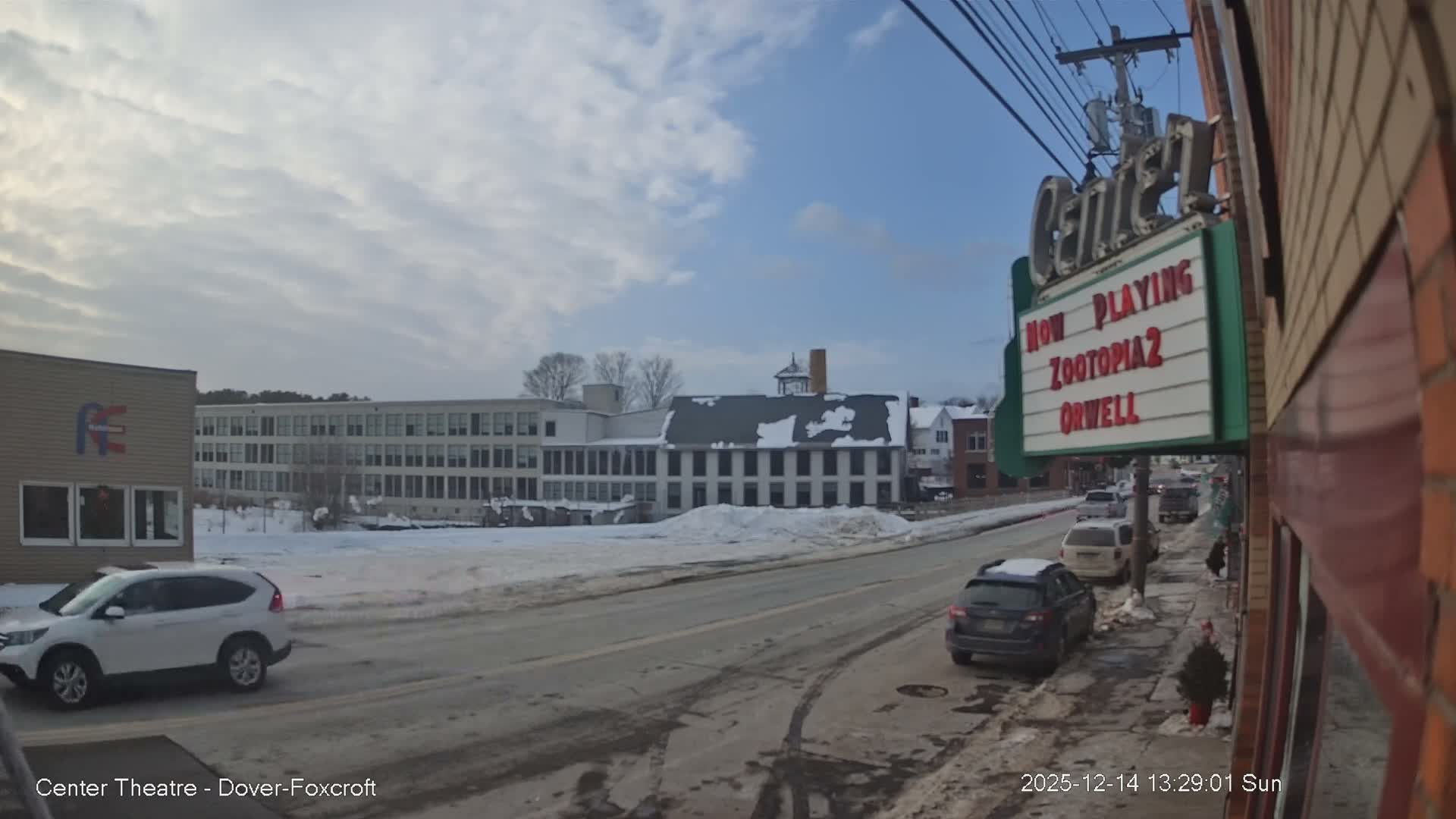 A cold, snowy winter night scene shows a brightly lit red neon sign on the right, overlooking a street with a car driving away and background buildings adorned with Christmas lights.