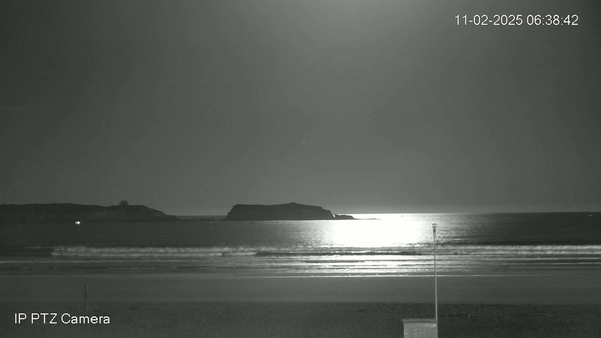A moonlit beach scene shows gentle waves lapping the shore, with a dark island silhouetted against the water.