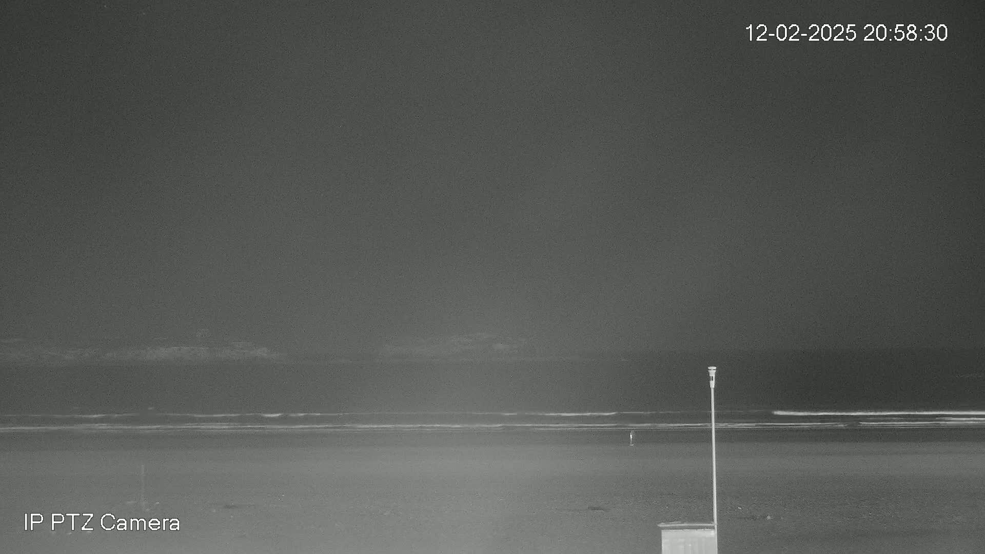 A nighttime beach scene shows a dark ocean with gentle waves under a clear, dark sky.