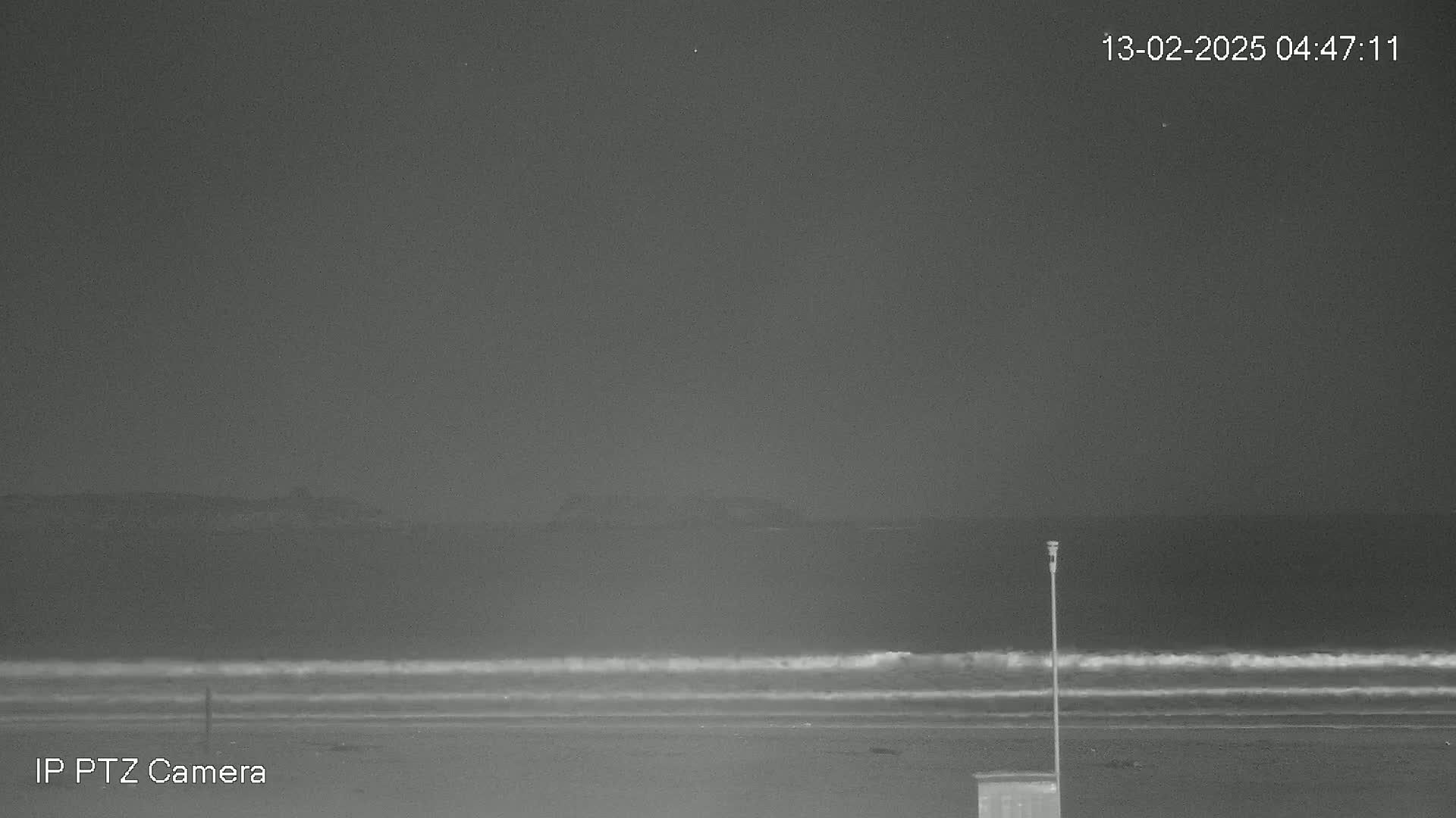 A dark, nighttime beach scene shows gentle waves lapping the shore under a clear sky.