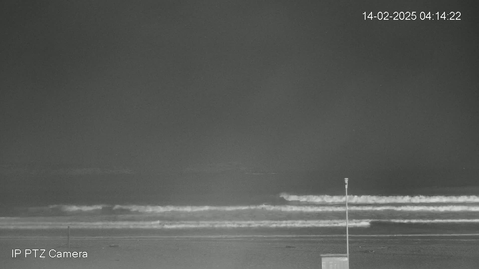 A nighttime, grayscale image shows several waves rolling onto a dark sandy beach under a dark sky.