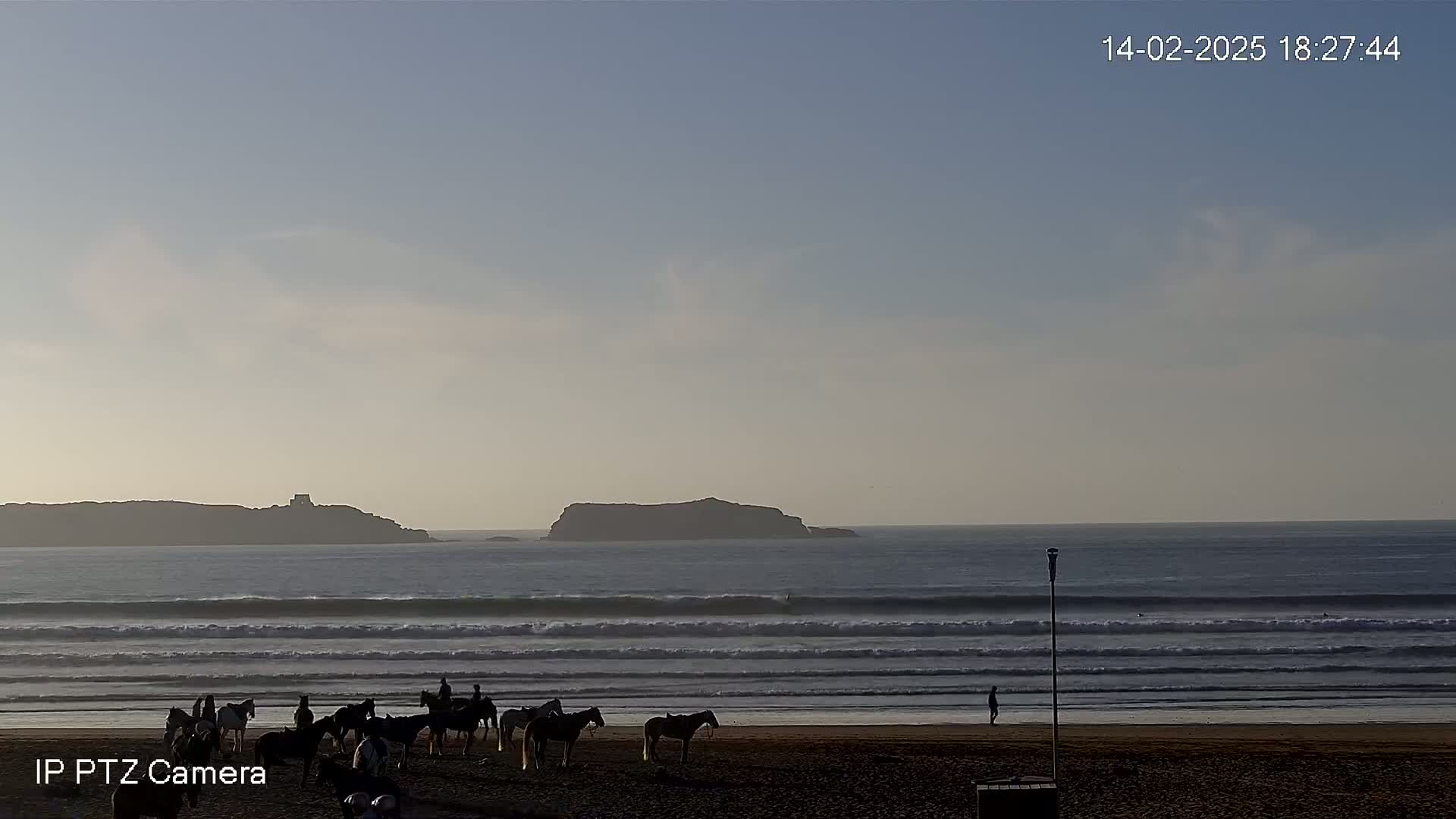 A sandy beach with several people riding horses is visible near calm ocean waves under a mostly clear sky.