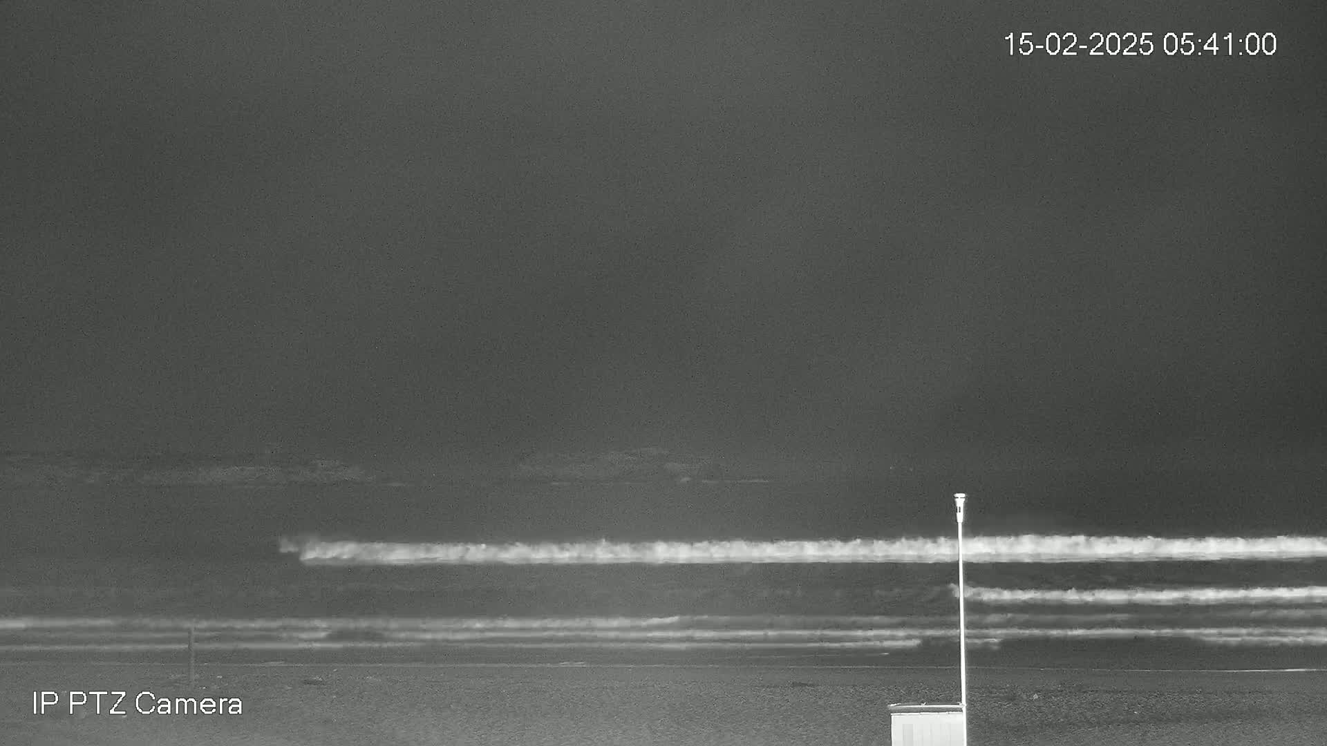 A dark, nighttime beach scene shows waves breaking on the shore under a cloudy sky.