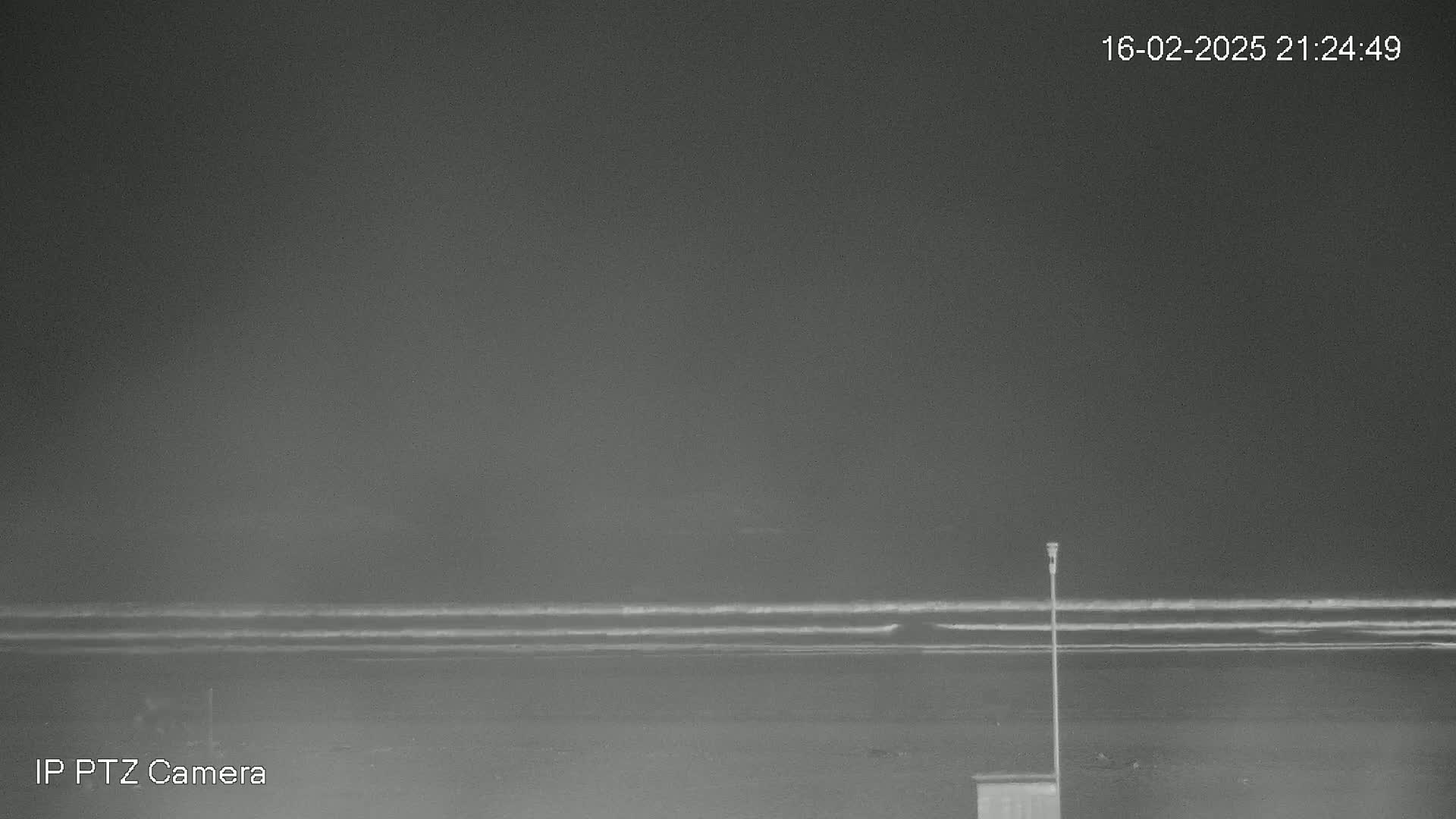 A nighttime, grayscale image shows a dark beach with small waves under a dark sky.