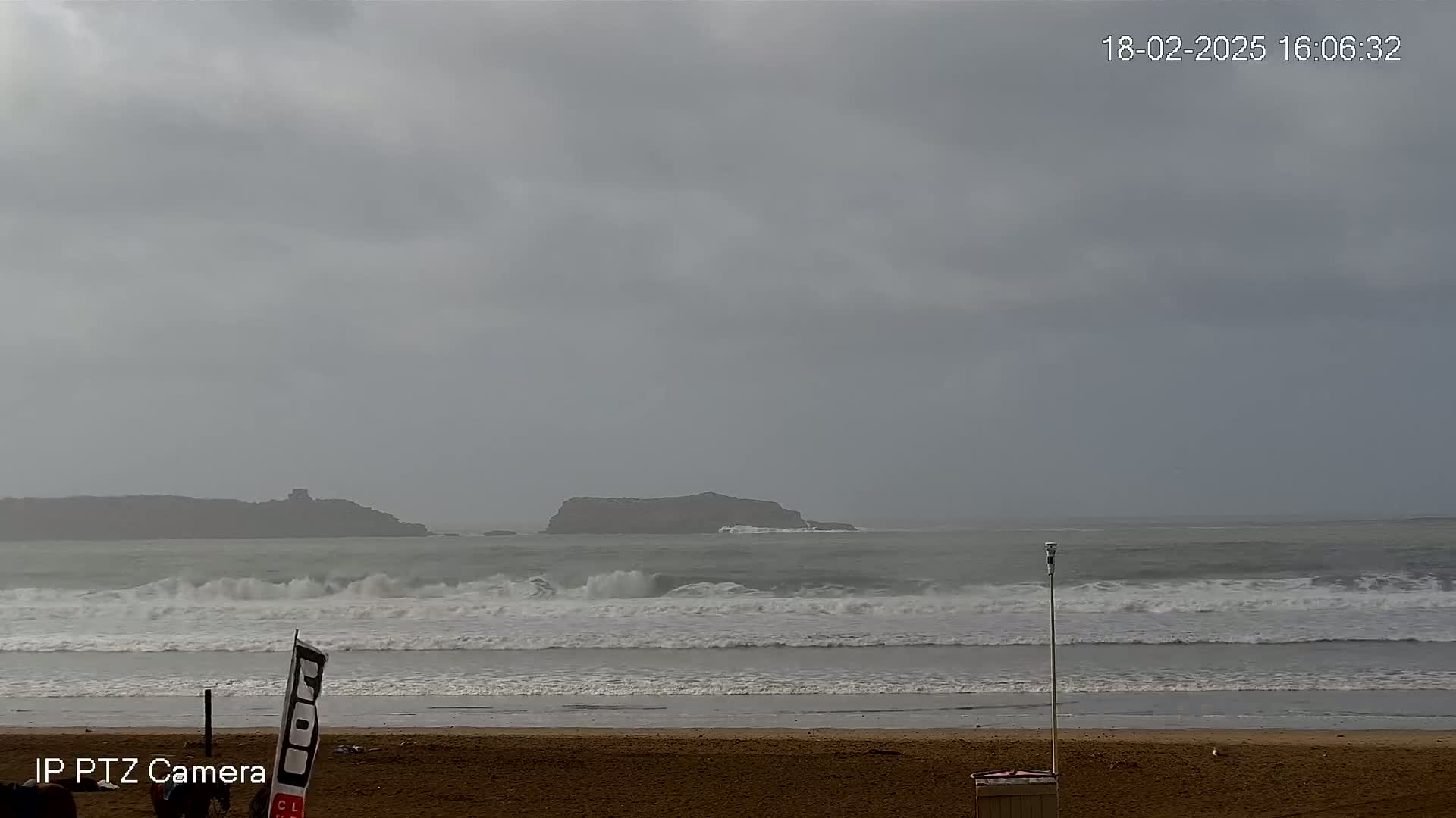 A sandy beach with moderately sized waves crashing on the shore under an overcast sky.