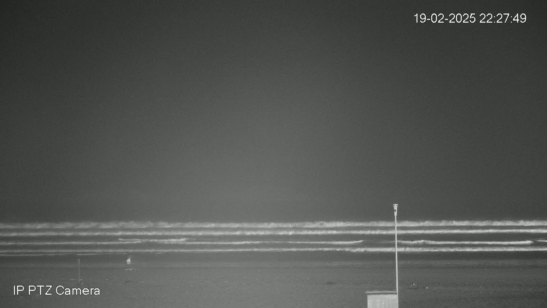 A nighttime beach scene shows a dark, overcast sky above gently rolling waves on a mostly empty shore.