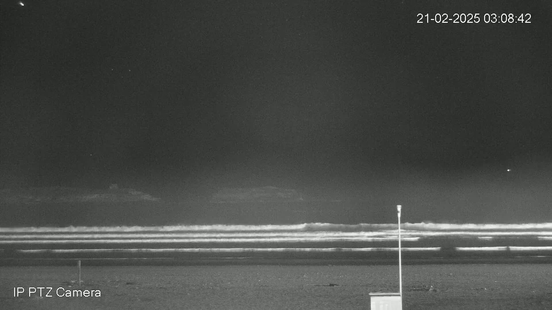 Under a dark night sky, waves roll onto a mostly empty beach.