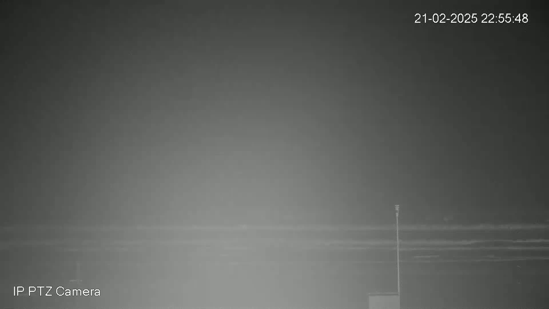 A hazy, nighttime scene shows a low horizon line with a single pole extending upward.