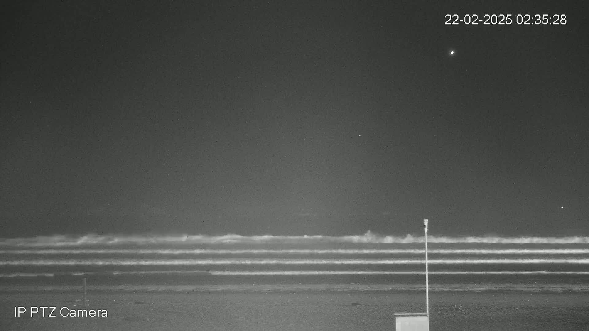 A nighttime beach scene shows moderately rough waves under a clear, dark sky.