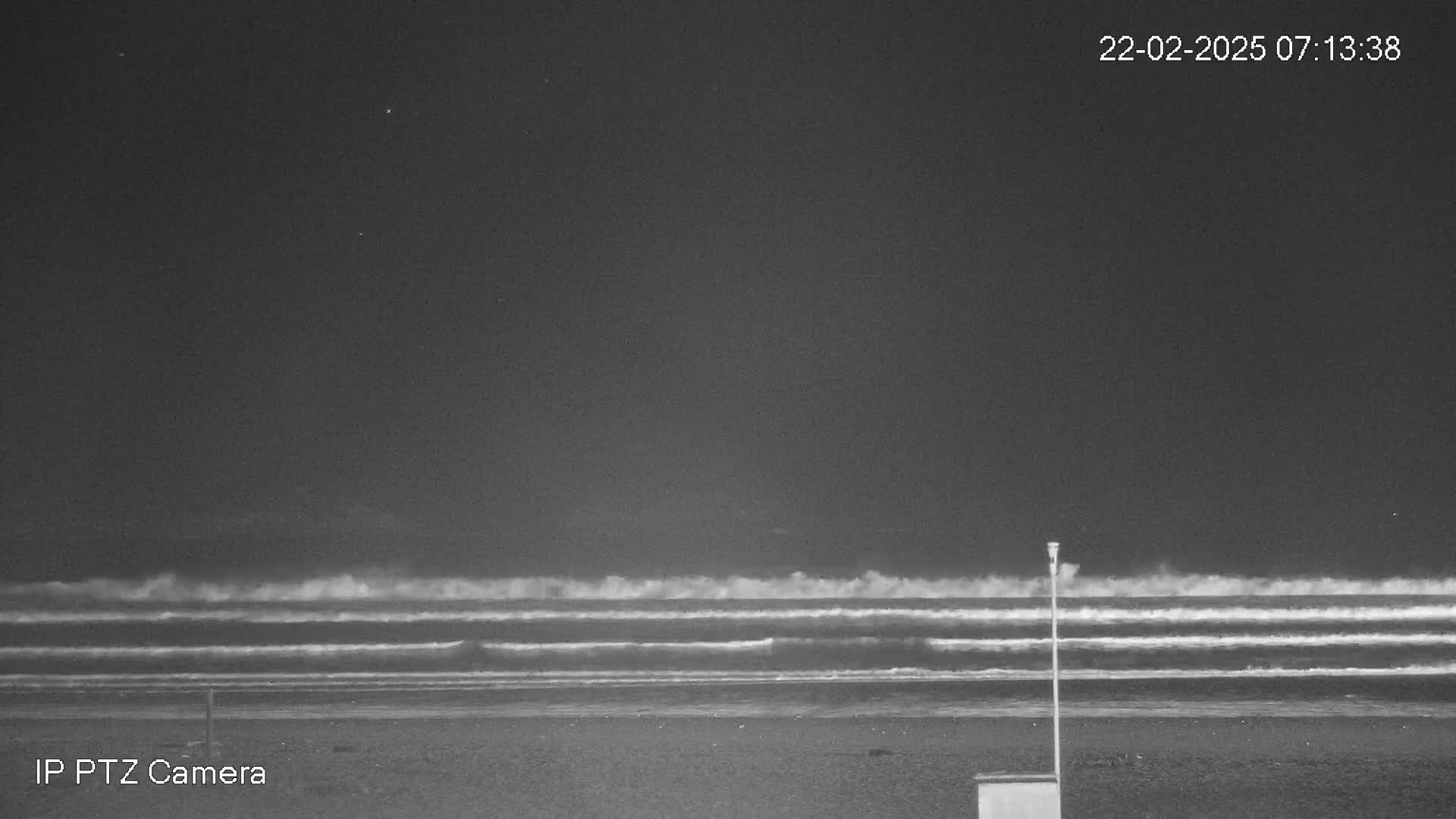 A dark, nighttime beach scene shows waves rolling onto the shore under a clear, starlit sky.