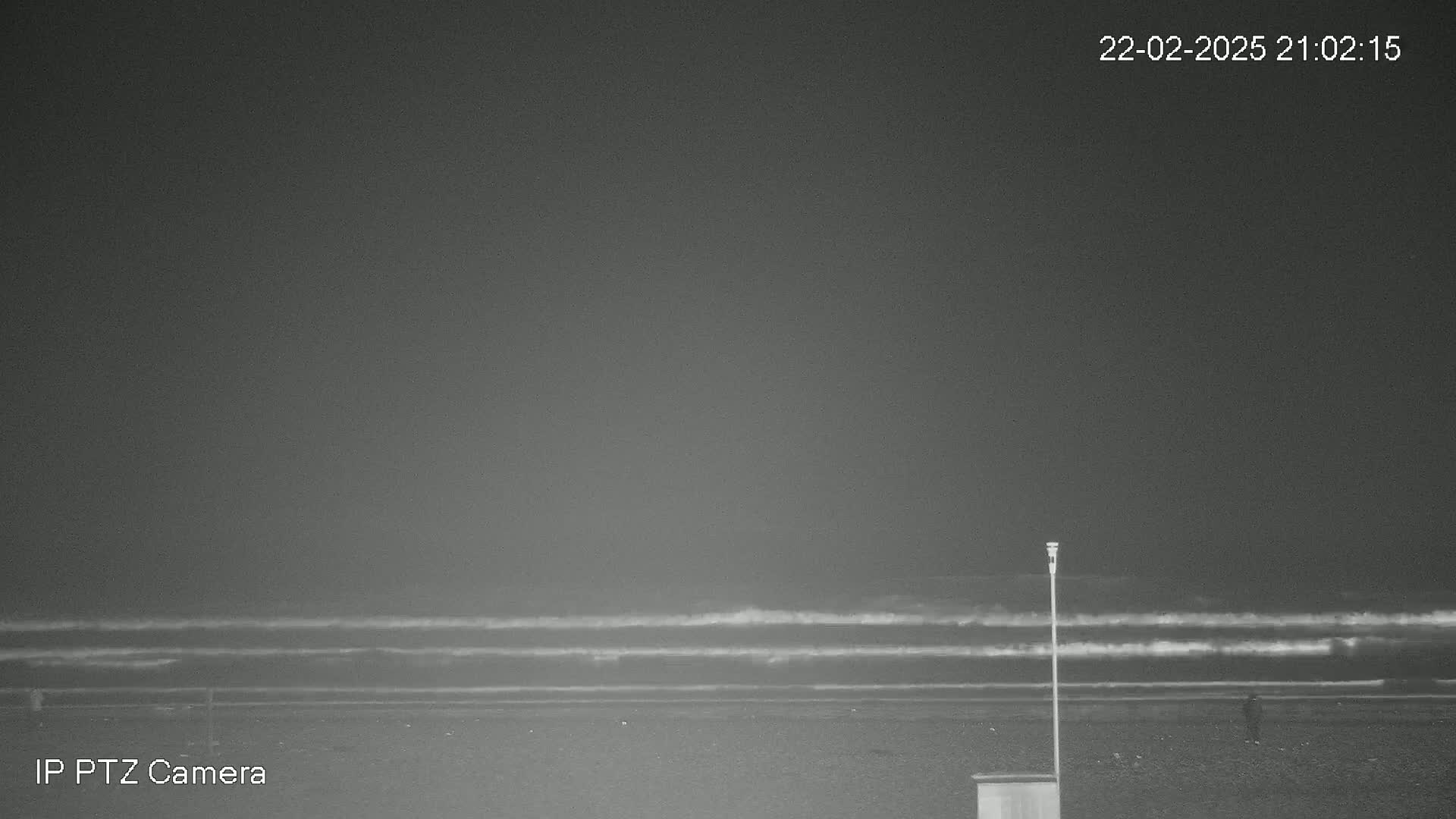 A dark, nighttime beach scene shows gentle waves lapping the shore under a cloudy sky.