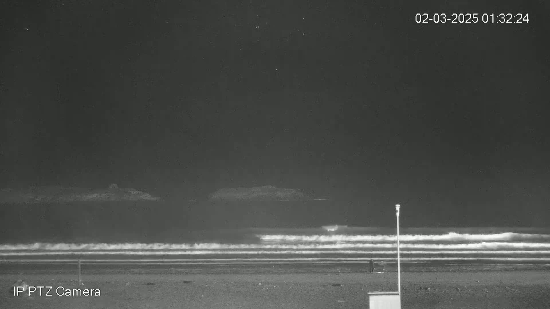 Under a dark night sky, gentle waves roll onto a mostly empty beach.