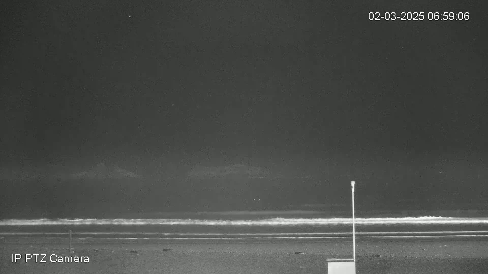 A dark, nighttime beach scene shows gently lapping waves under a mostly clear sky.