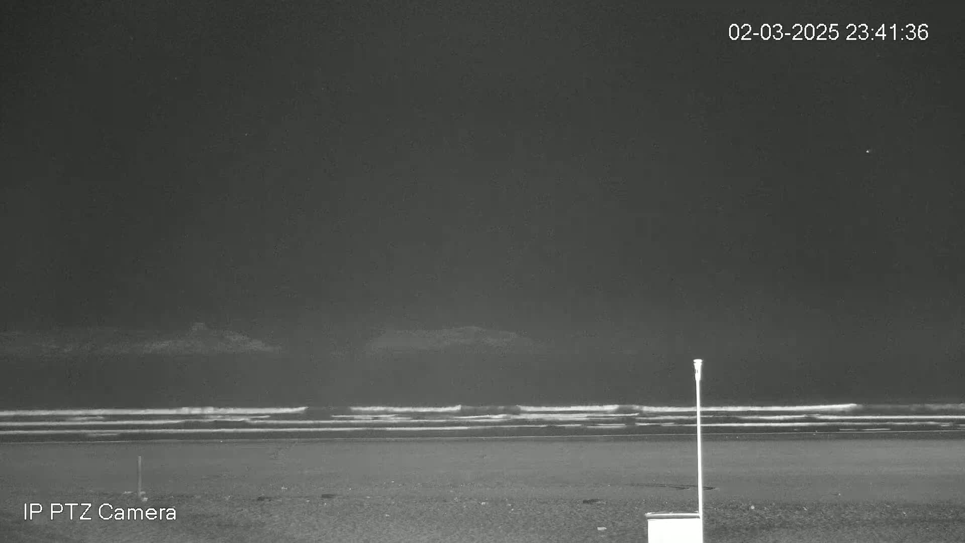 A dark nighttime beach scene shows gently rolling waves on the ocean under a clear sky.