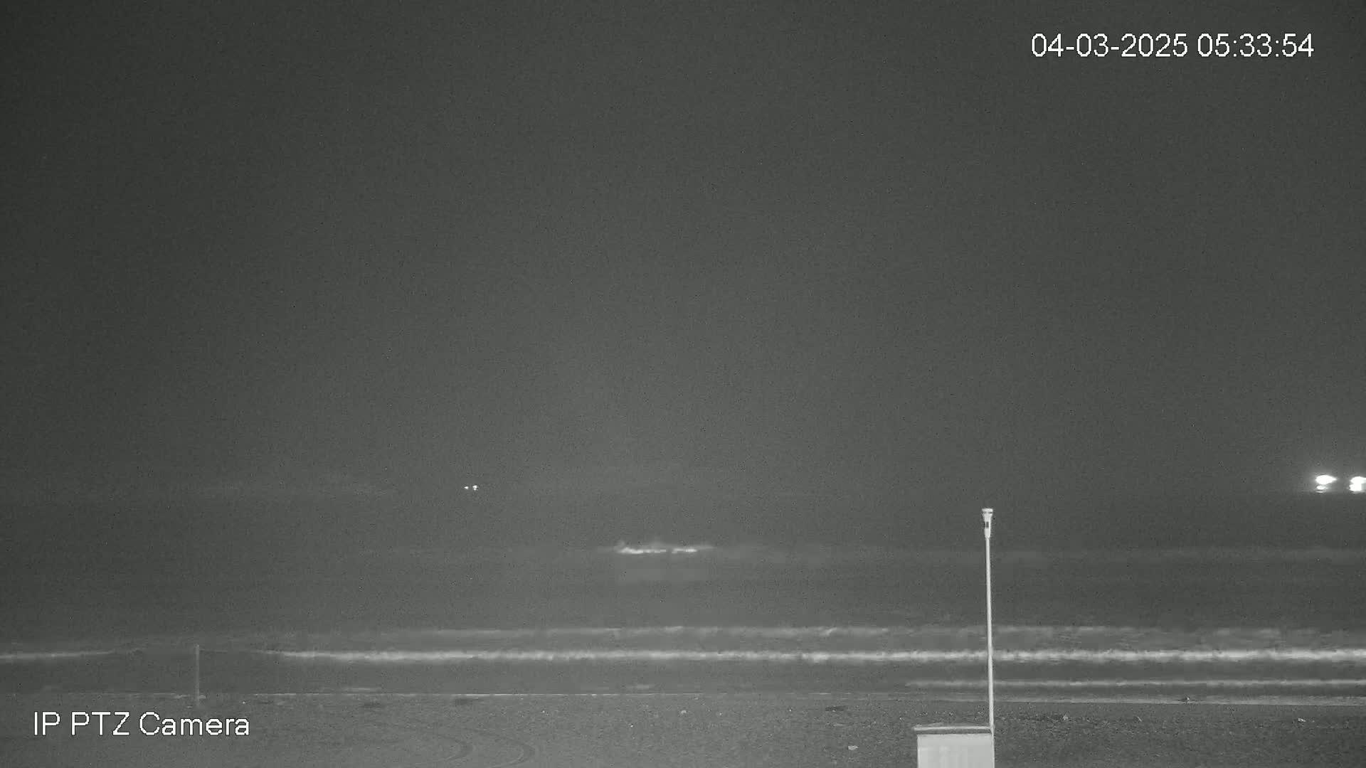 A dark, nighttime beach scene shows a gently lapping ocean under a cloudy sky.