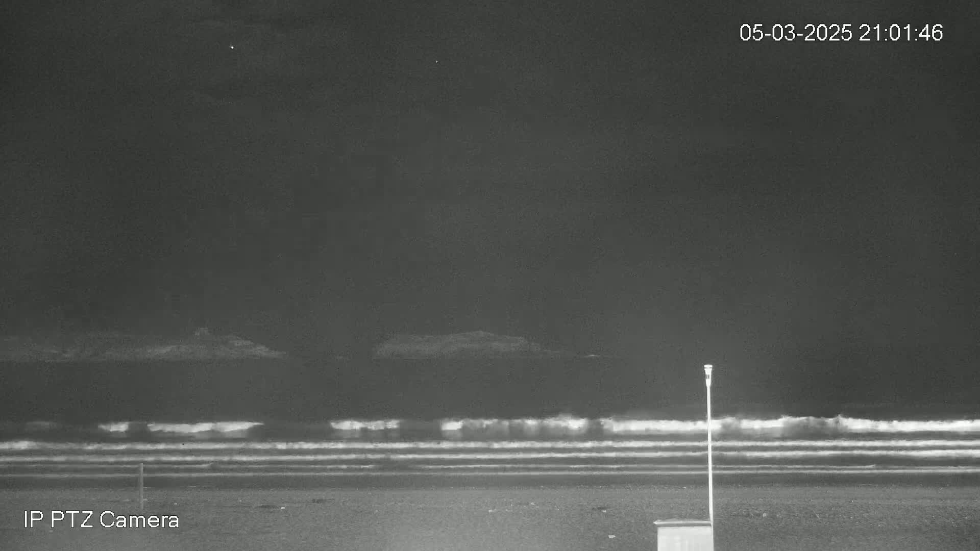 A dark, nighttime beach scene shows gently rolling waves under a clear sky.