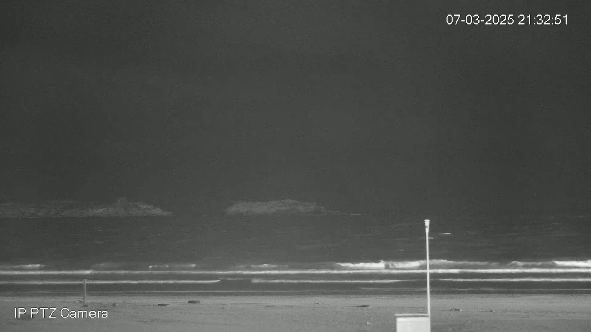 A nighttime beach scene shows dark, wavy water under a dark sky.