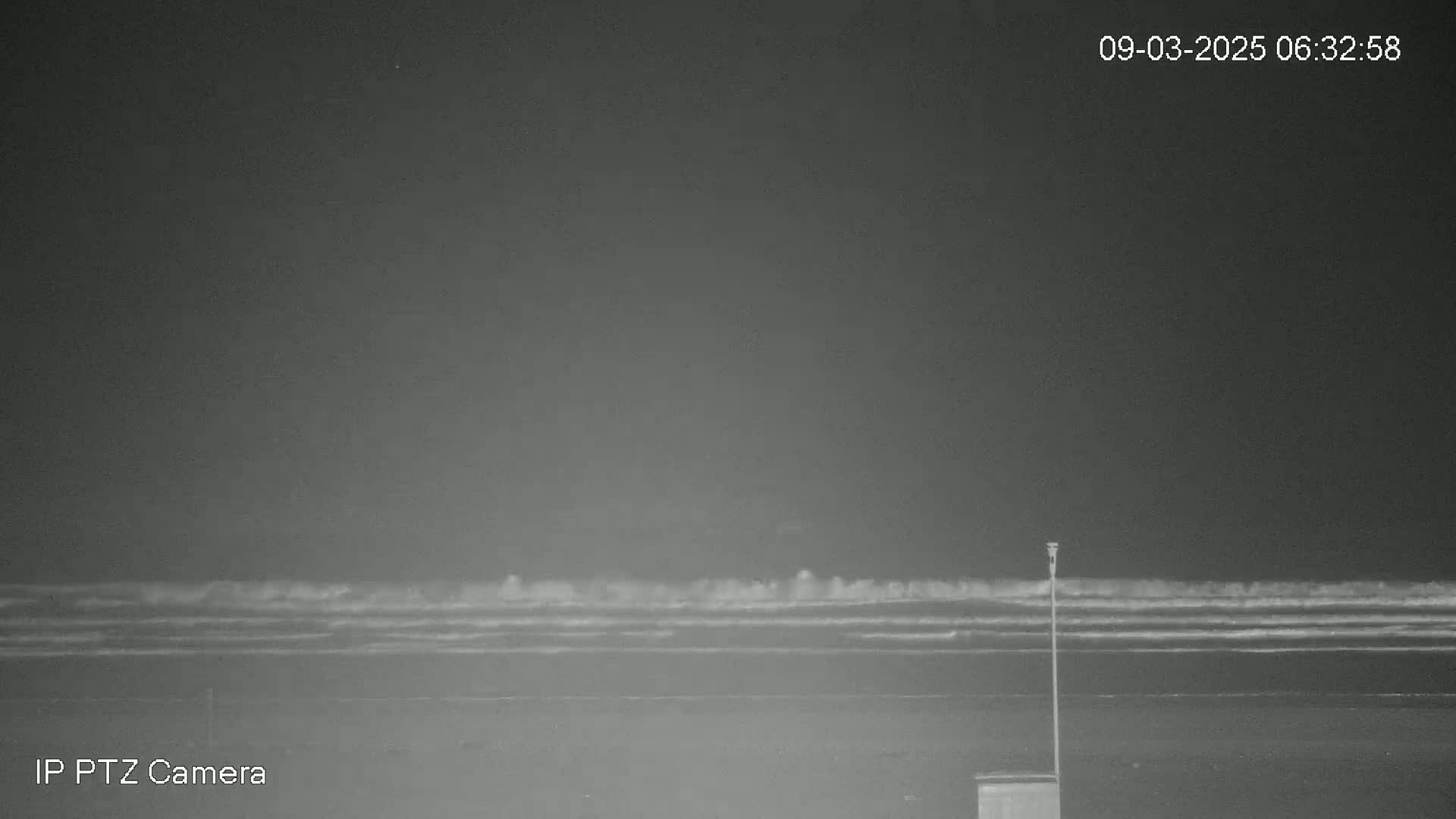 A dark, nighttime beach scene shows gentle waves lapping the shore under a cloudy sky.