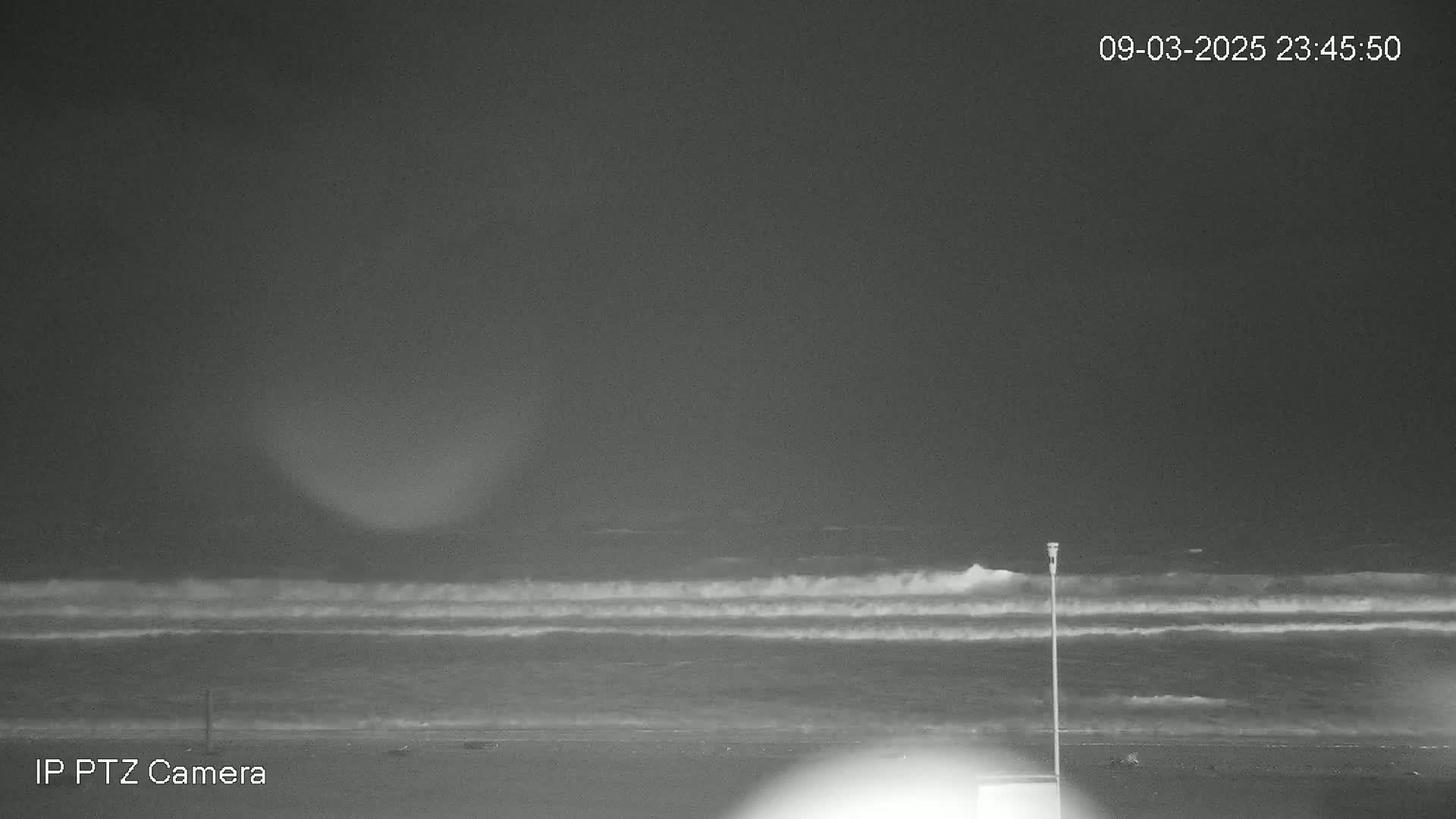 A nighttime beach scene shows waves breaking on the shore under a dark, overcast sky.